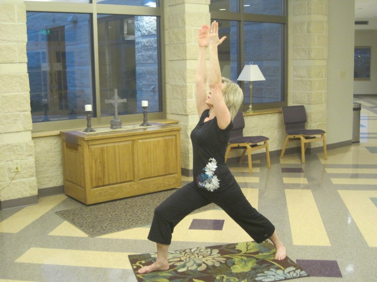 WholyFit Certified Instructor performing “Overcomer” pose in a church building with a Christian cross in the background, 2011. Courtesy Erin Garvey. An instructor performing "Overcomer" pose.