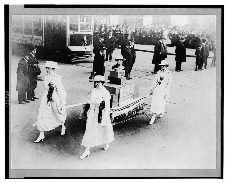 Photograph shows four women carrying ballot boxes on a stretcher during a suffrage parade in New York City, New York.
