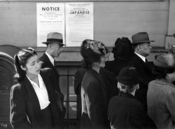 Japanese Americans in front of poster with internment orders