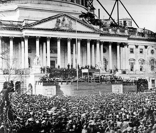 Abraham Lincoln's first inauguration which took place in Washington, DC. Lincoln stands underneath the covering at the center of the photograph. The scaffolding at upper right was being used in construction of the Capitol dome.