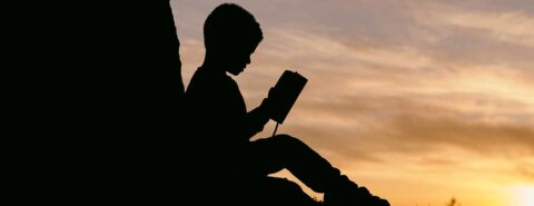 Silhouette of a child reading a book to illustrate the blog post "Five Children’s Classics That Stand the Test of Time [reading list]" on the OUP blog