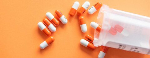 A photo of orange and white medication pills spilling across an orange background to illustrate the blog post "Alzheimer's: do we focus too much on new treatments?" by Paul T. Menzel, co-author of "Bioethics: What Everyone Needs to Know®" published by Oxford University Press