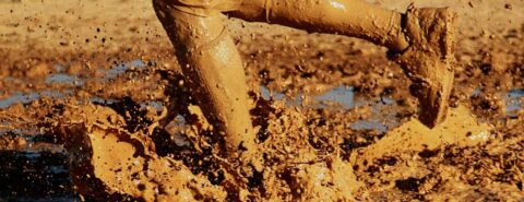 Photo of a person's mud-splattered legs running through a deep muddy puddle for the concept of "common as muck" as discussed in the blog post "Irregular gleanings and a last shot at Modern English usage" by the Oxford Etymologist on the OUP blog