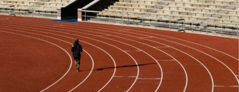 Man running laps on a track in an empty stadium.