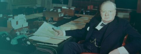 Image of Winston Churchill sitting at his desk holding a paper.