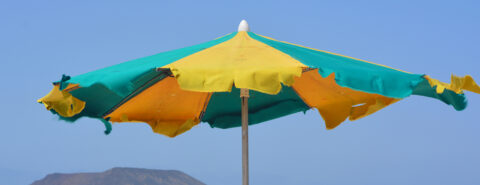 A tattered beach umbrella with yellow and green panels against a clear blue sky.