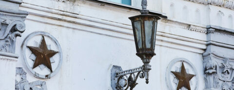 Ornate street lamp on a building with star emblems and decorative moldings.