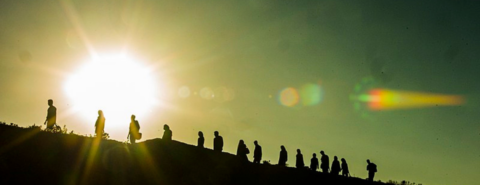 Silhouettes of migrants walking along a path, carrying belongings with the sun in the background