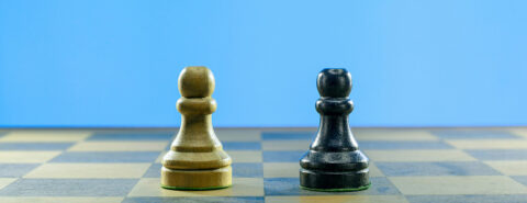 Two chess pieces, white and black pawns, on top of a chess board and clean solid blue background