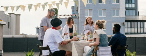 A group of friends having lunch on a rooftop with a blue building in the background.