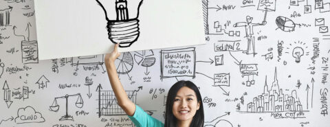 Woman Holding up a drawing of a Light bulb on a White Board