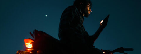 A man sitting with a cellphone on a Motorbike at night.