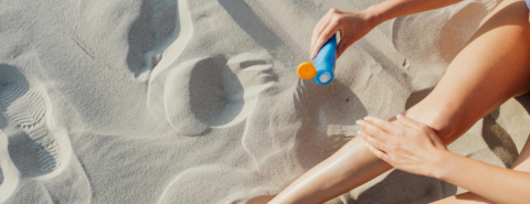 Close up of woman applying sunscreen to bare legs on a sandy beach