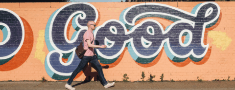 A person walking in front of a street art mural that reads "Good" in large letters
